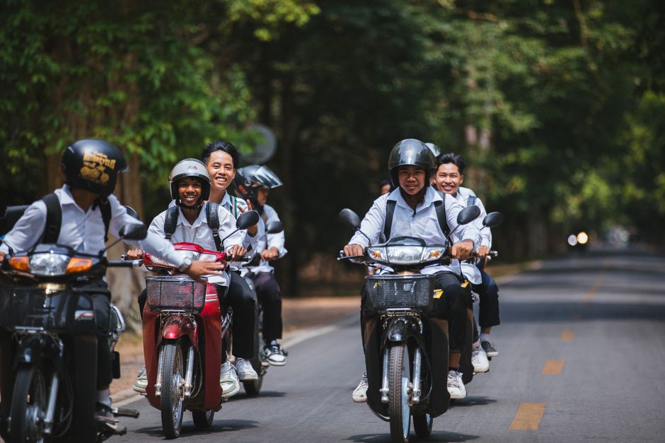 Group of teenagers joyfully riding scooters on a sunny day in Siem Reap, Cambodia.