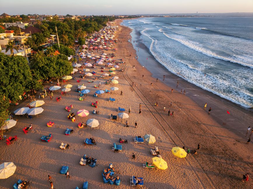 Aerial shot of lively beach with colorful umbrellas and ocean waves in Bali, Indonesia.