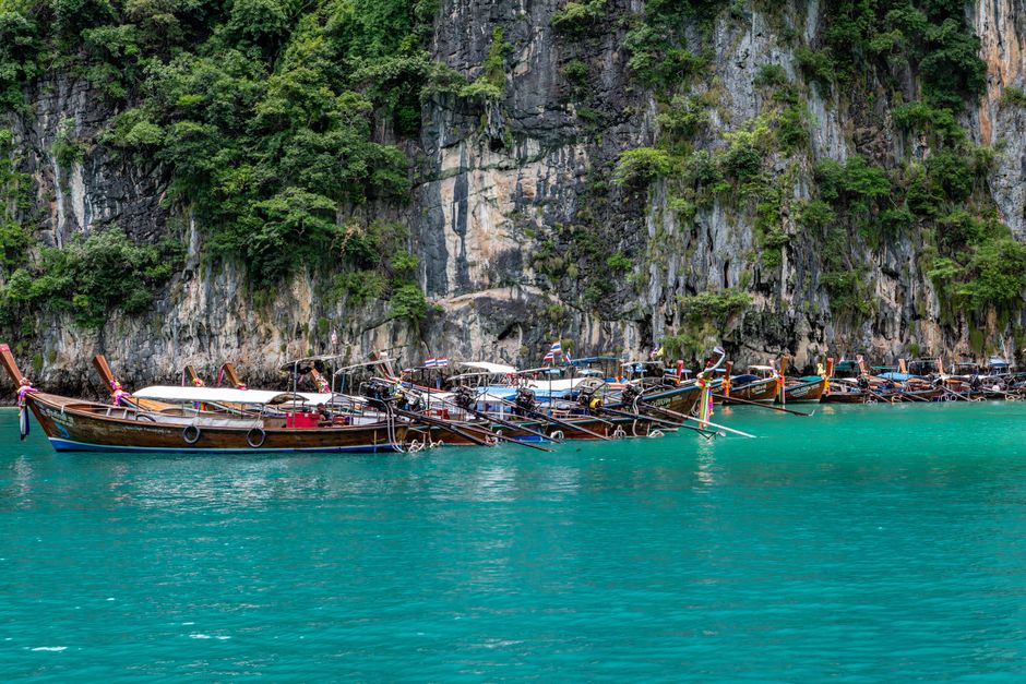 Scenic view of traditional longtail boats moored against cliffs in Phuket, Thailand's turquoise waters.