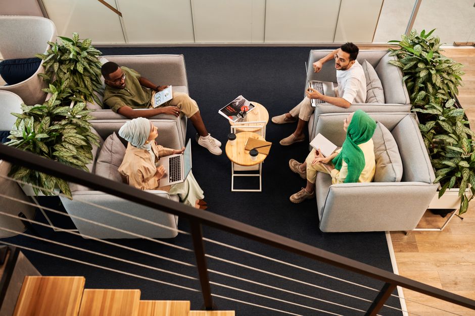 Overhead view of a diverse team engaging in a meeting in a modern office lounge area with laptops.