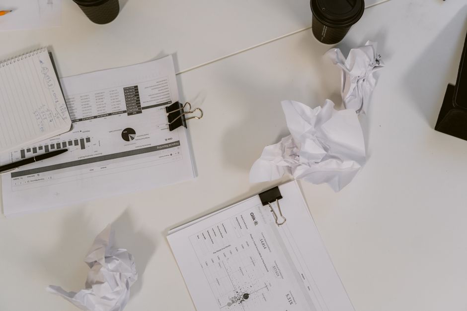 An overhead view of a desk filled with business documents, crumpled paper, and coffee cups.