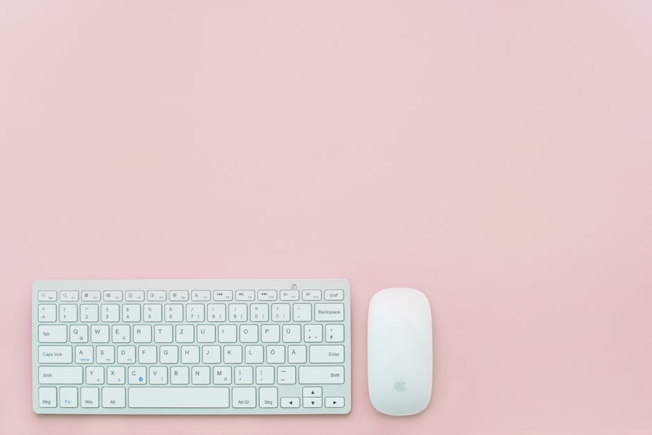 A clean and minimalist flat lay of a white keyboard and mouse on a pastel pink background. Perfect for feminine office themes.