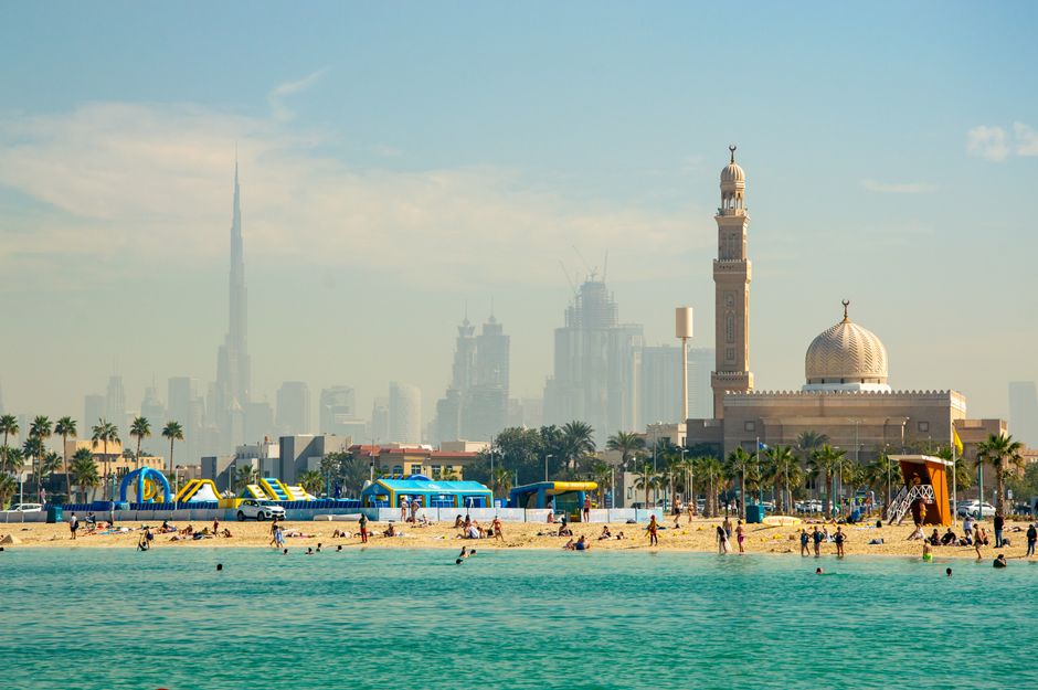 Lively Dubai beach scene with the iconic Burj Khalifa and traditional mosque in the background.
