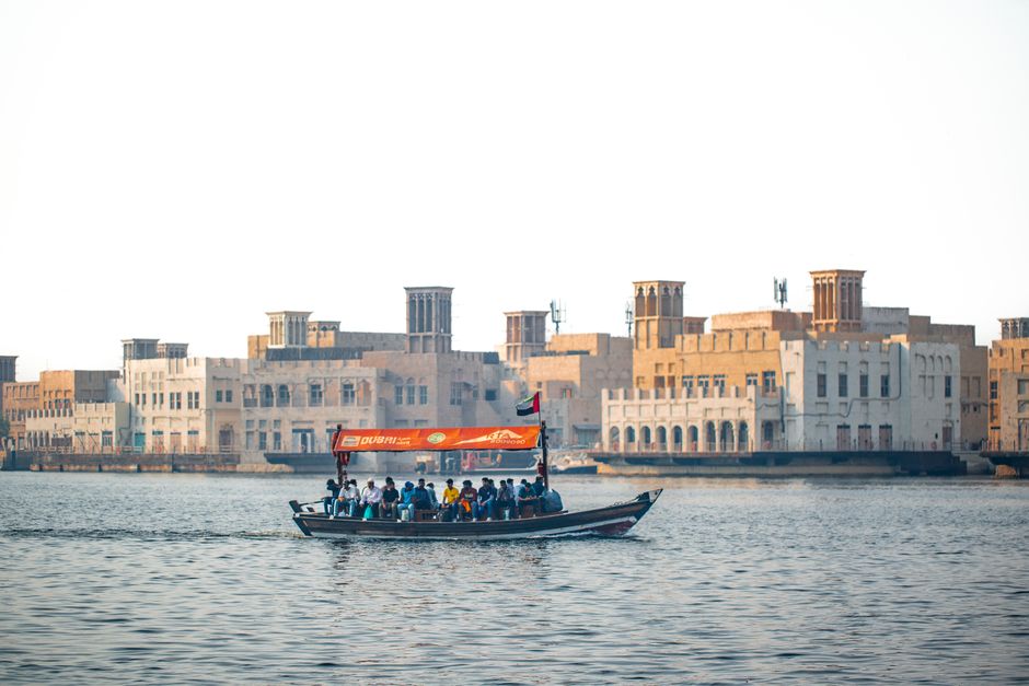 Traditional boat crossing Dubai Creek with historical architecture in the backdrop.