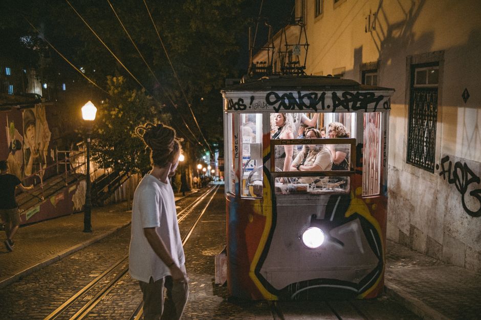 Street scene in Lisbon at night featuring a vintage tram and pedestrians, capturing urban life.