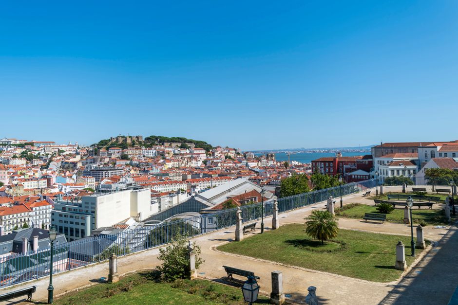 Elevated view of Lisbon skyline and São Jorge Castle under blue skies, from a park.