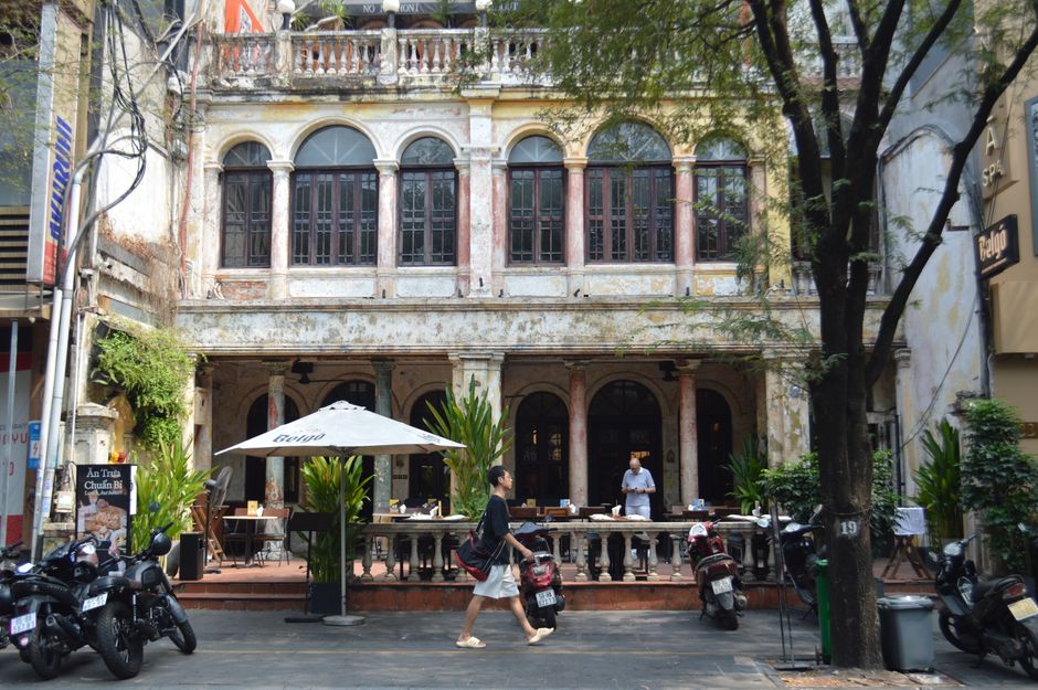 A man walks past a charming historic café with outdoor seating and vintage architecture.