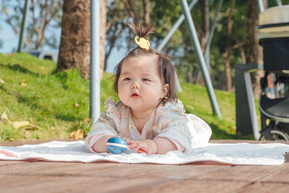 Cute toddler enjoying sunny day outdoors, lying on a blanket with a toy.