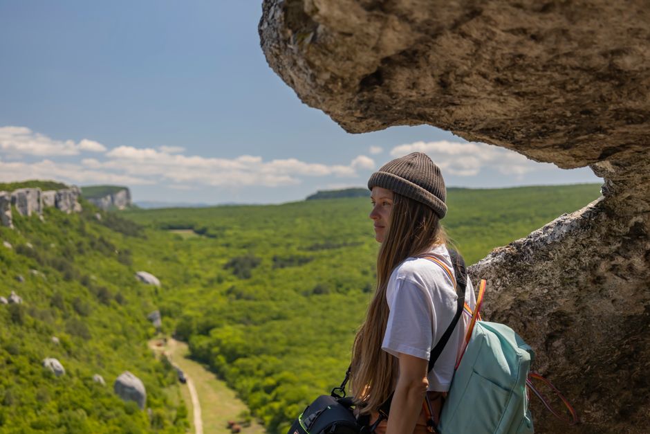 Woman hiking on a cliffside with a vast green landscape in view, perfect for adventure travel themes.