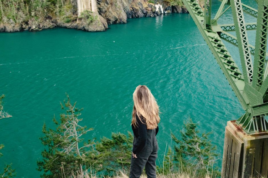 Woman overlooking serene ocean from a rocky, green cliff. Perfect travel inspiration.