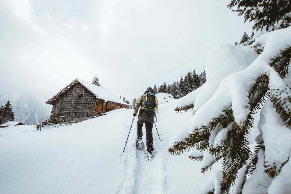 Hiker on snowy mountain path toward a cabin