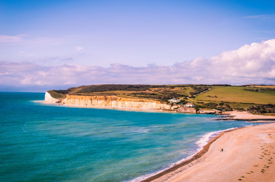 A breathtaking aerial view of Eastbourne's coastline, showcasing cliffs, turquoise waters, and sandy beach under a clear summer sky.