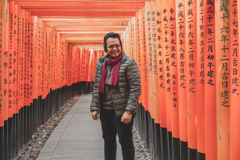 A man standing happily among the red torii gates at Fushimi Inari Taisha, Kyoto, Japan.