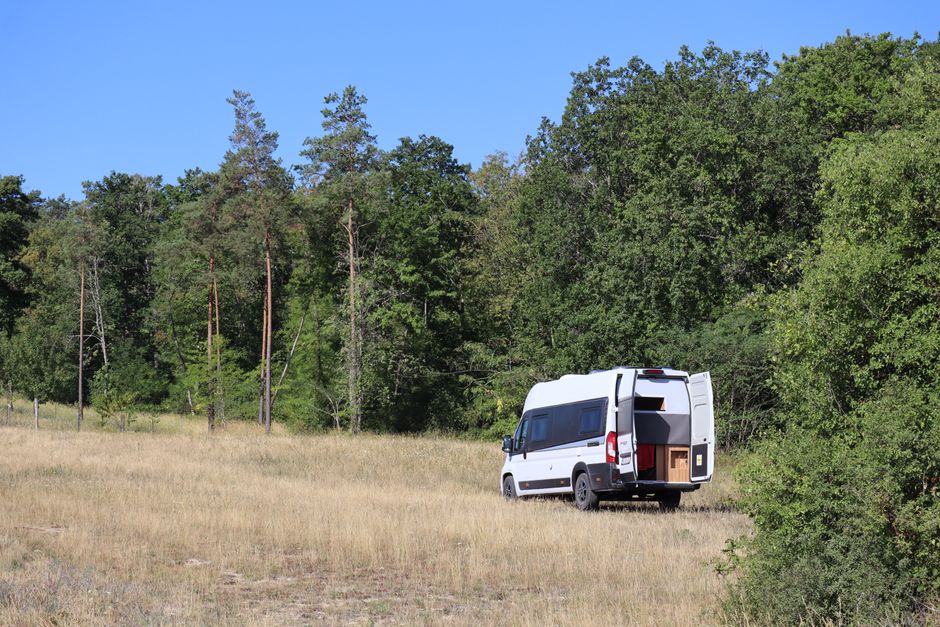 White campervan parked in a grassy area near a forest in Fralignes, Grand Est, France.