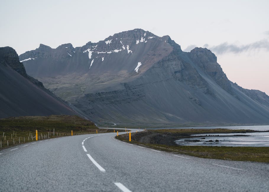 A winding road leading through Icelandic mountains, offering a serene and picturesque landscape at dusk.