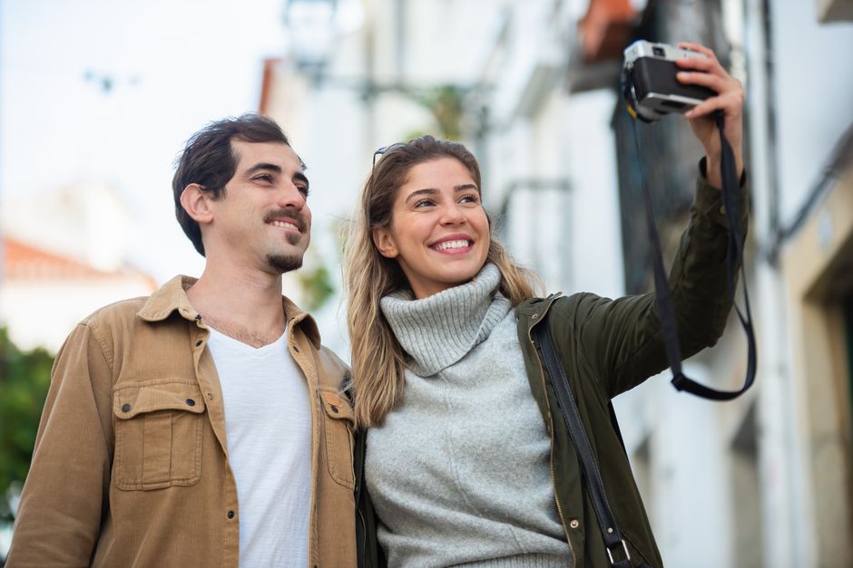 Smiling couple taking a photo together outside, enjoying a lovely autumn day.