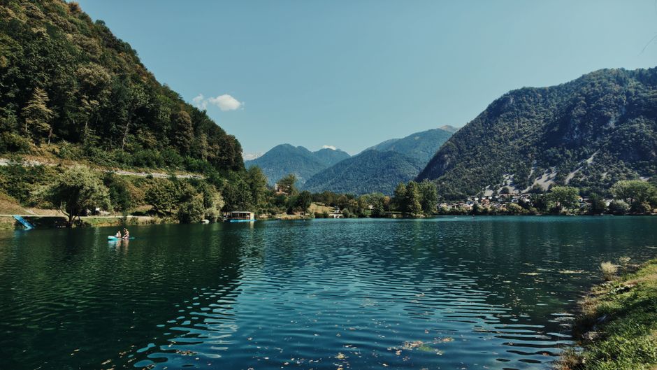 Peaceful lake surrounded by lush mountains and clear blue sky, offering a scenic view.