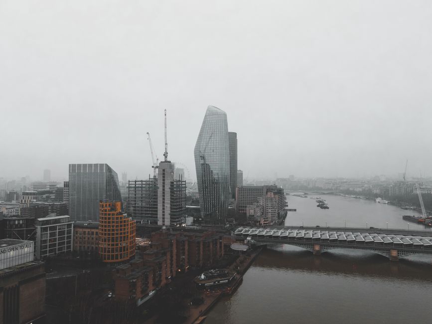 Aerial view of city with bridge on river near modern buildings under gray cloudy sky in foggy day