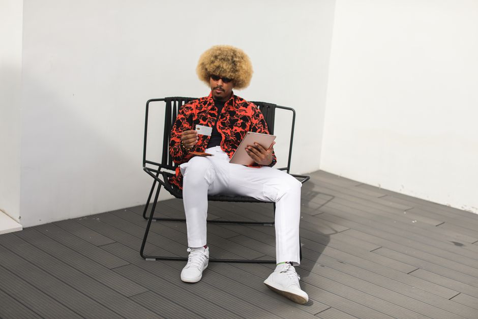 Stylish man with afro making online purchase using a tablet while sitting on a chair.