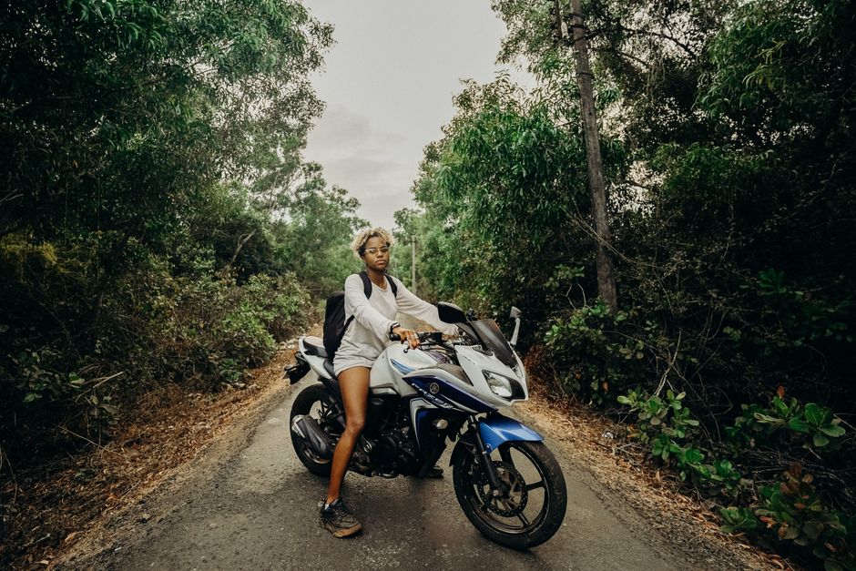 A young woman rides a motorcycle through a lush jungle road, exuding adventure and freedom.