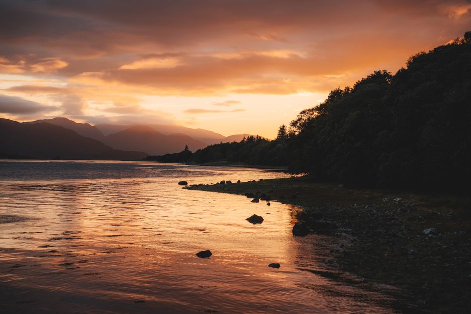 Sunset over a serene Scottish loch with mountains