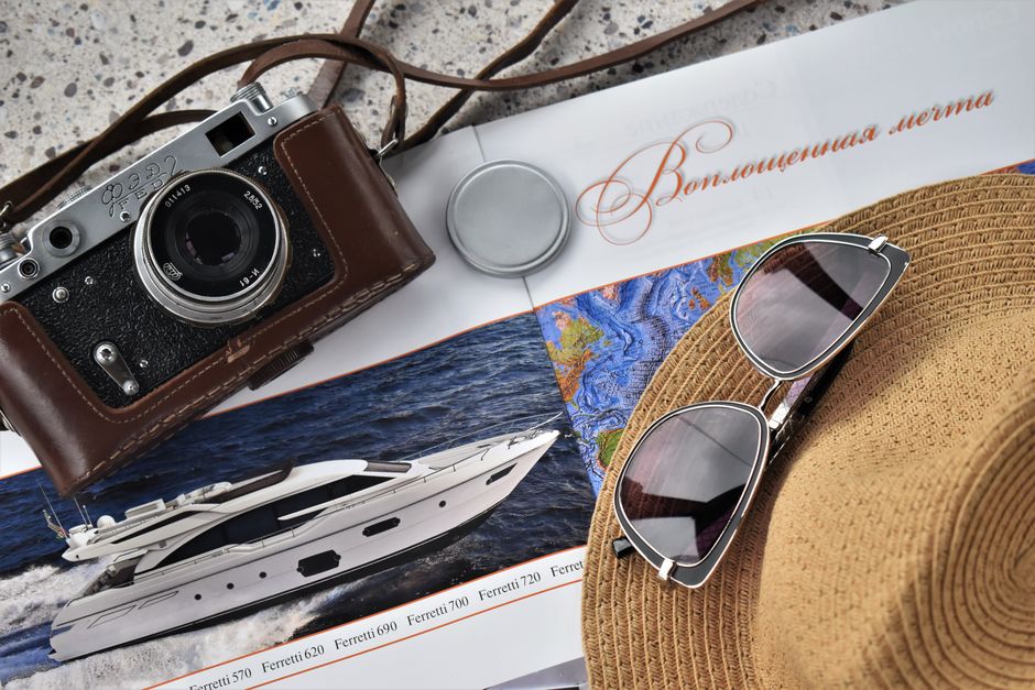 A flat lay of a vintage camera, sunglasses, and travel magazine with a yacht image.