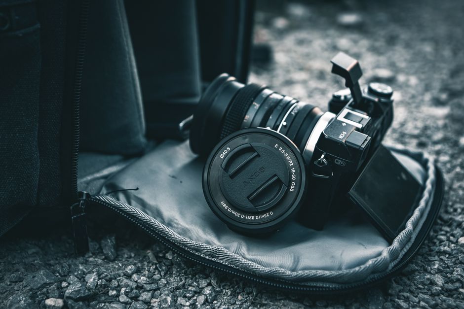 Close-up of a mirrorless camera resting on a gray bag on gravel.