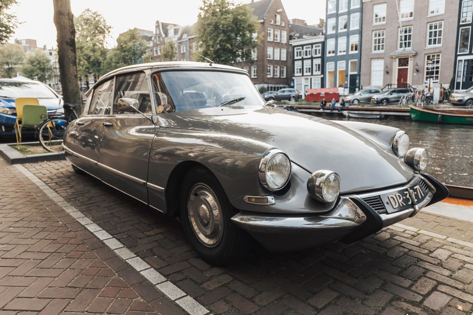 A classic Citroen DS vintage car parked beside a picturesque canal in Amsterdam under daytime light.