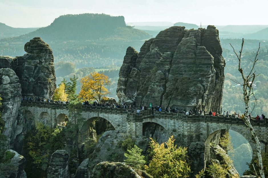 Explore the iconic Bastei Bridge surrounded by stunning rocks and autumn foliage in Saxony, Germany.