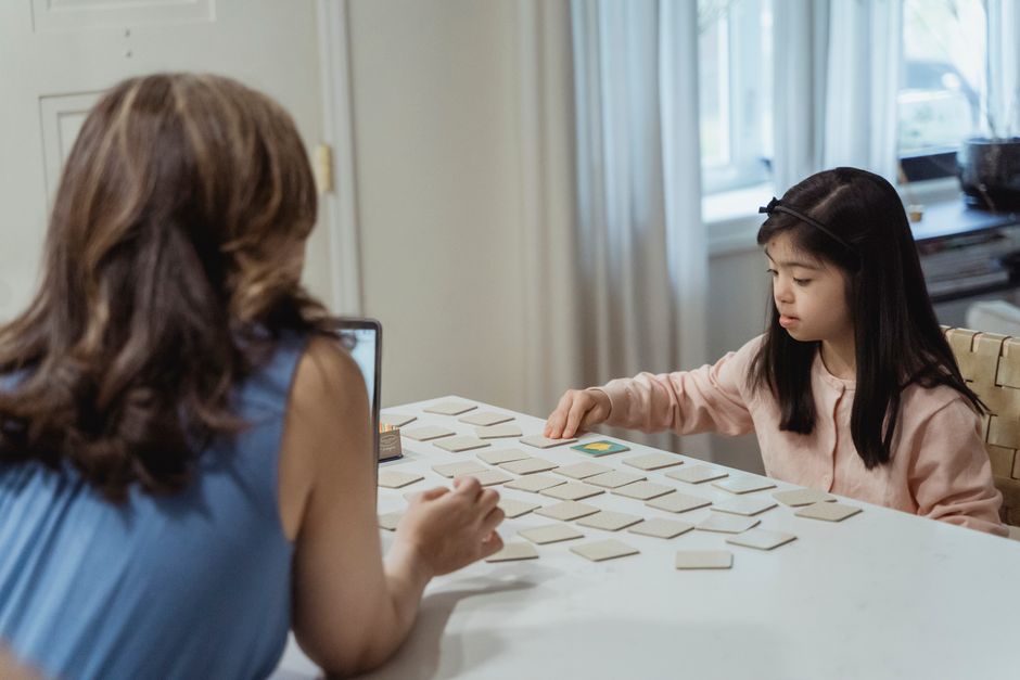 A young girl and her mother play a card game on a white table, fostering family time.