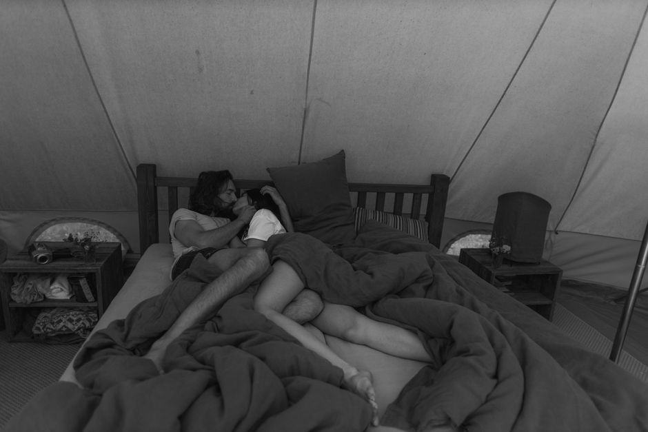 Intimate scene of a couple cuddling in a tent bed, evoking warmth and connection.
