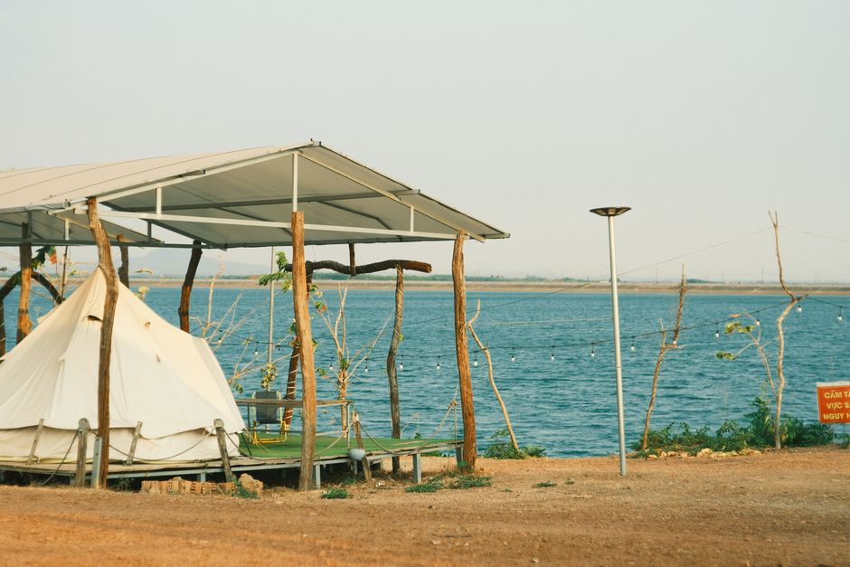 Peaceful lakeside camping scene with a tent under a canopy by the water.