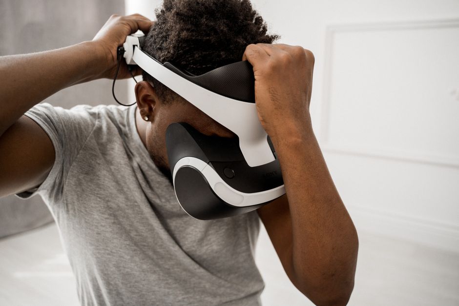 A man in a gray shirt adjusting his virtual reality headset inside a bright room.